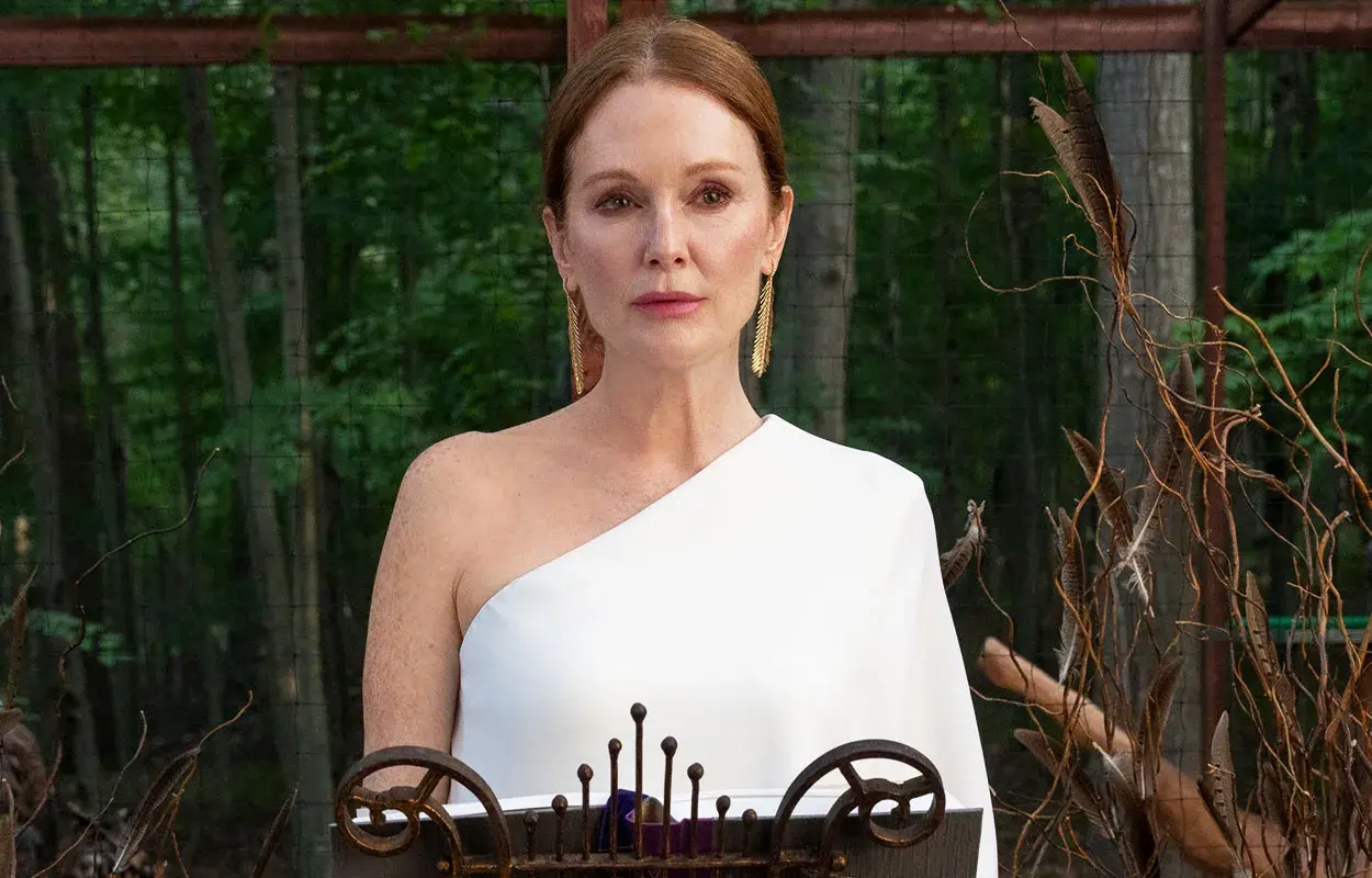 Julianne Moore i den vita klänningen i "Sirens"-serien, med en bakgrund av skog och dekorativa kvistar.