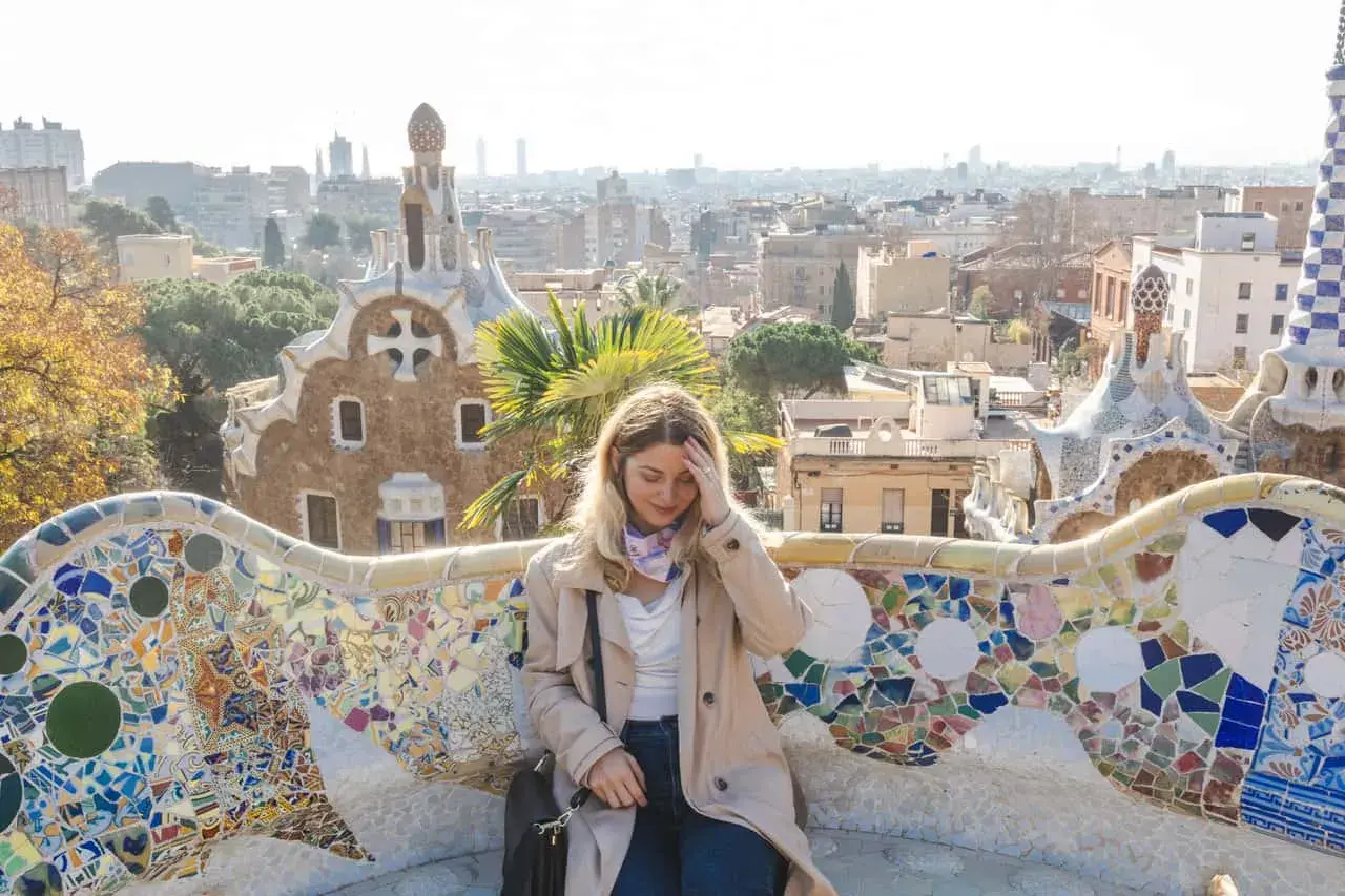 Frau sitzt auf einer bunten Mosaikbank im Park Güell, mit Blick auf Barcelona. Tolle Barcelona Tipps für deinen Besuch!