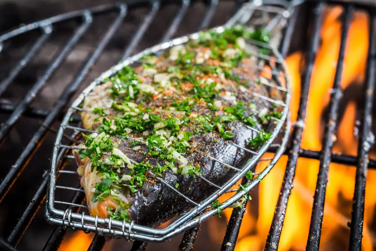 Poisson entier assaisonné d'herbes et d'épices, sur une grille de barbecue avec des flammes vives. Le temps de cuisson du poisson au barbecue est crucial pour un résultat parfait.