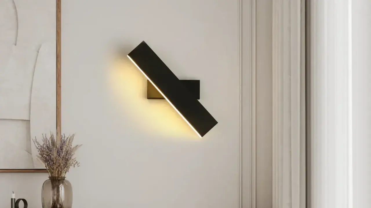 Moderna lámpara de pared negra con luz LED cálida, ilumina un rincón acogedor junto a un jarrón con flores secas.