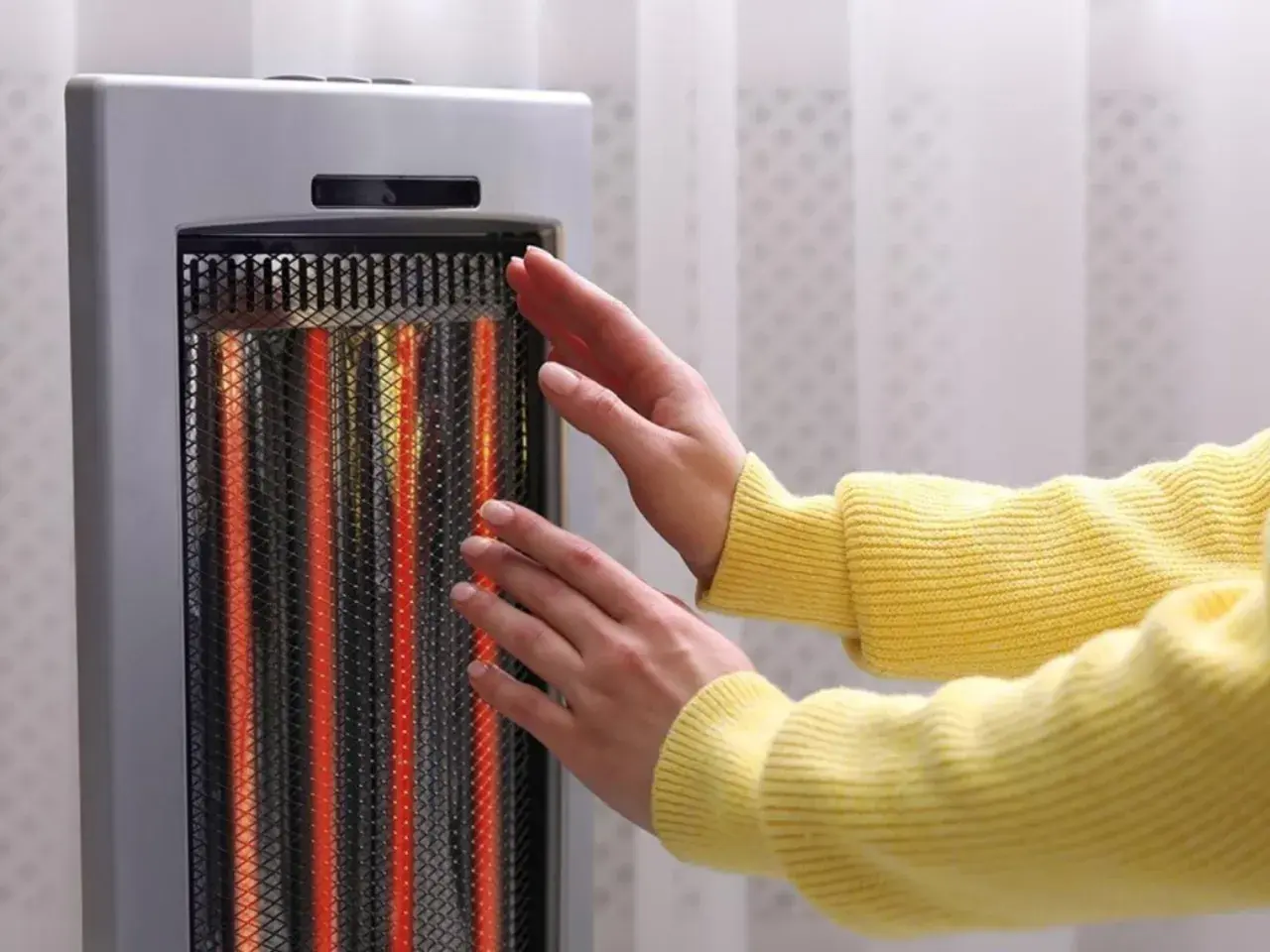 Manos cerca de un calentador eléctrico encendido. Las estufas eléctricas son peligrosas, ¡mantén la distancia!