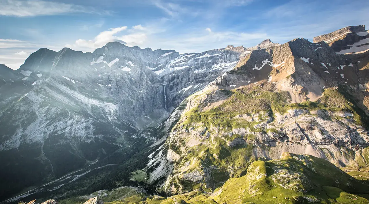 Le cirque de Gavarnie, majestueux amphithéâtre naturel, dévoile ses falaises abruptes, une cascade lointaine et des pentes verdoyantes sous un ciel bleu.