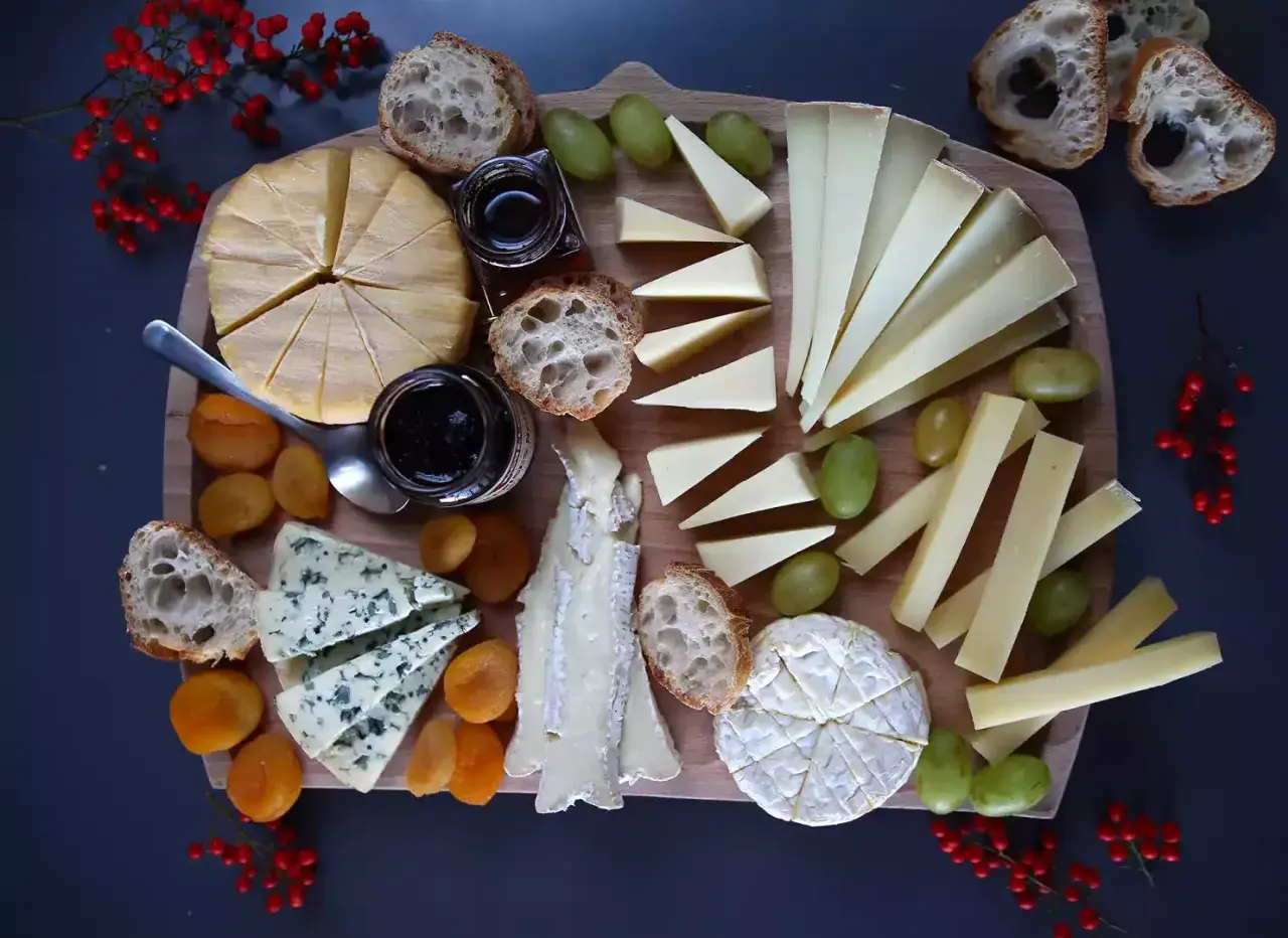 Un tagliere ricco di formaggio di capra francese, accompagnato da pane croccante, uva, albicocche secche e marmellata.
