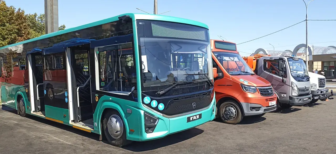 Nowe autobusy i samochody dostawcze stoją obok siebie. Jeden z autobusów, w kolorze turkusowym, ma otwarte drzwi, gotowy do podróży z Augustowa do Łodzi.