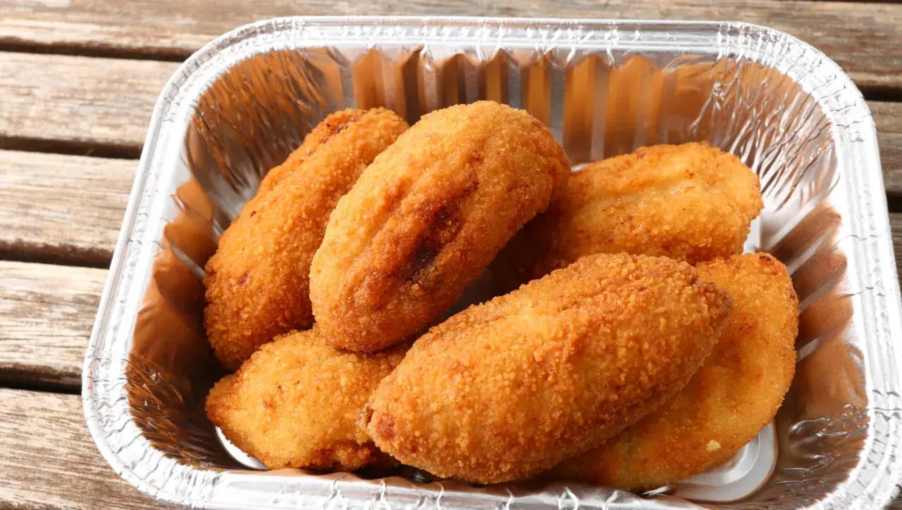 Croquetas de pollo doradas y crujientes en un recipiente de aluminio, listas para disfrutar.