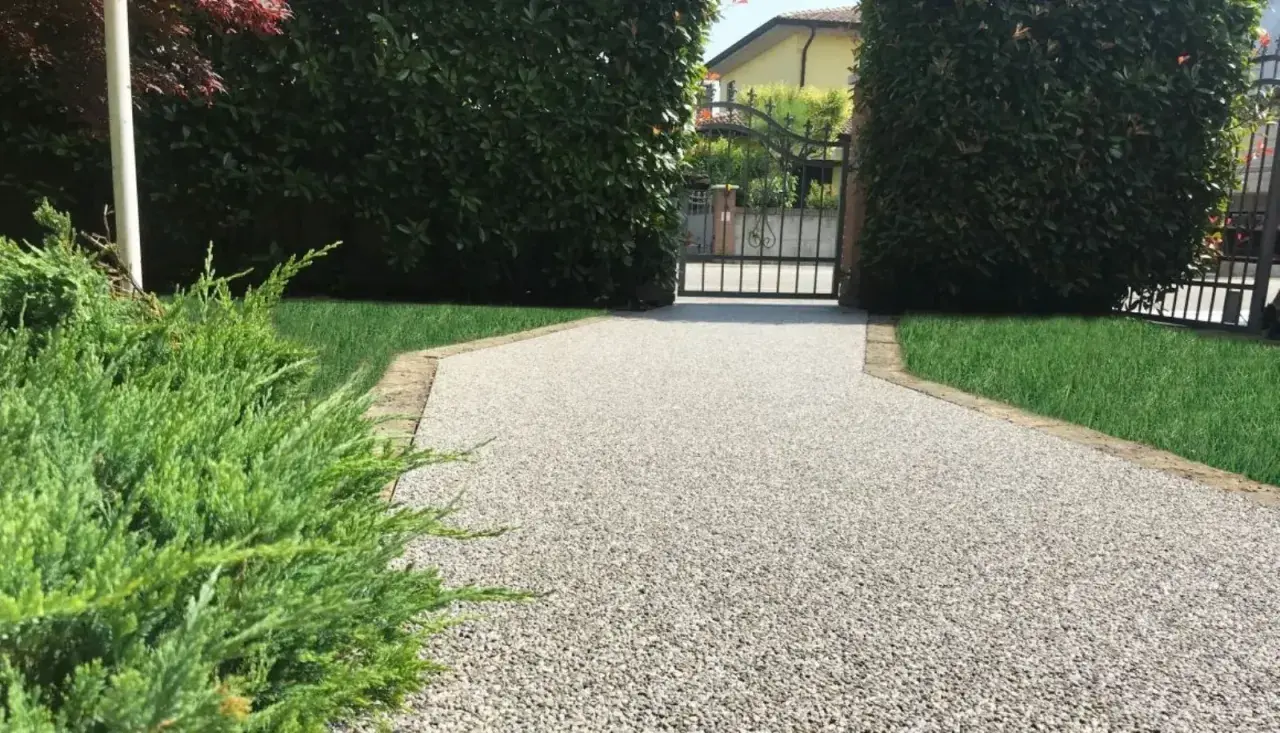 Vialetto carrabile in pietra, con ghiaia chiara e bordi in cotto, conduce a un cancello in ferro battuto.