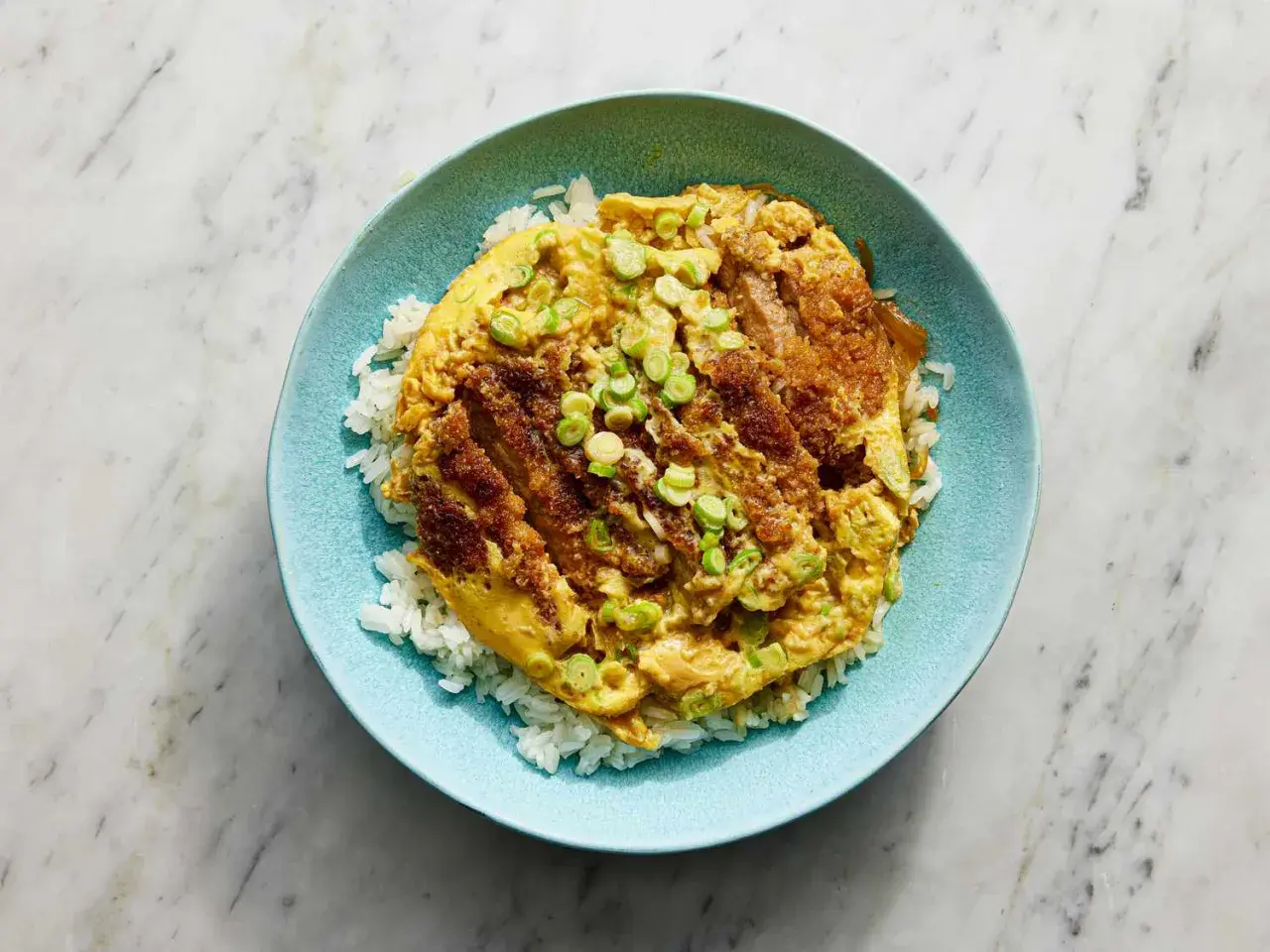 A delicious katsu donburi recipe, featuring crispy fried pork cutlet over fluffy white rice, topped with a savory egg and green onions.