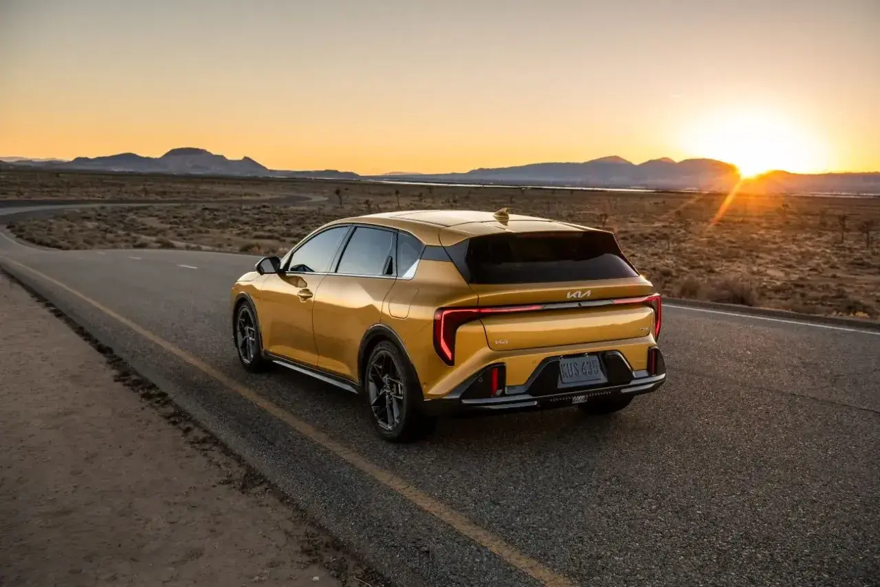 Un coche hatchback amarillo brillante recorre una carretera desierta al atardecer, con las montañas al fondo.