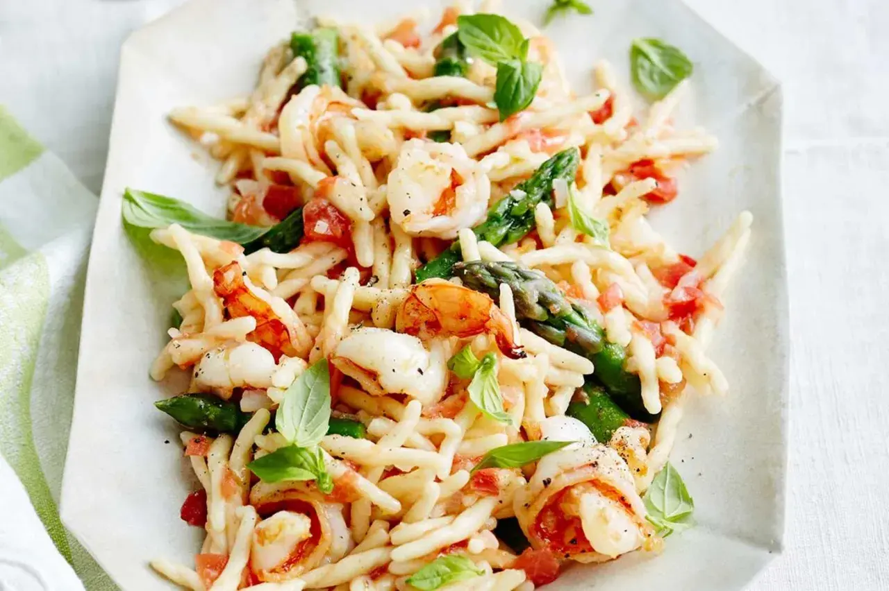 Trofie-Pasta mit Garnelen, Spargel und Tomaten, garniert mit Basilikum.