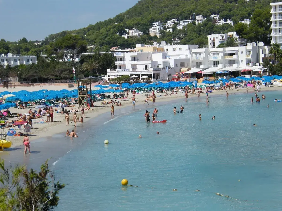 Lloret de Mar, lipiec: słoneczna pogoda zachęca do plażowania. Tłumy ludzi kąpią się i opalają na piaszczystej plaży, pod błękitnymi parasolami.