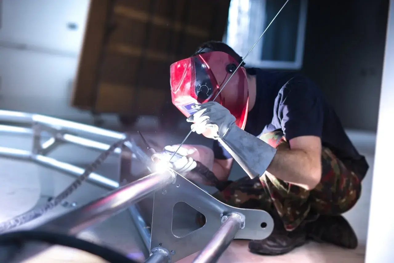 Spawacz w masce spawa aluminiową ramę. Widać jasny łuk spawalniczy i iskry. To pokazuje, czym spawać aluminium.