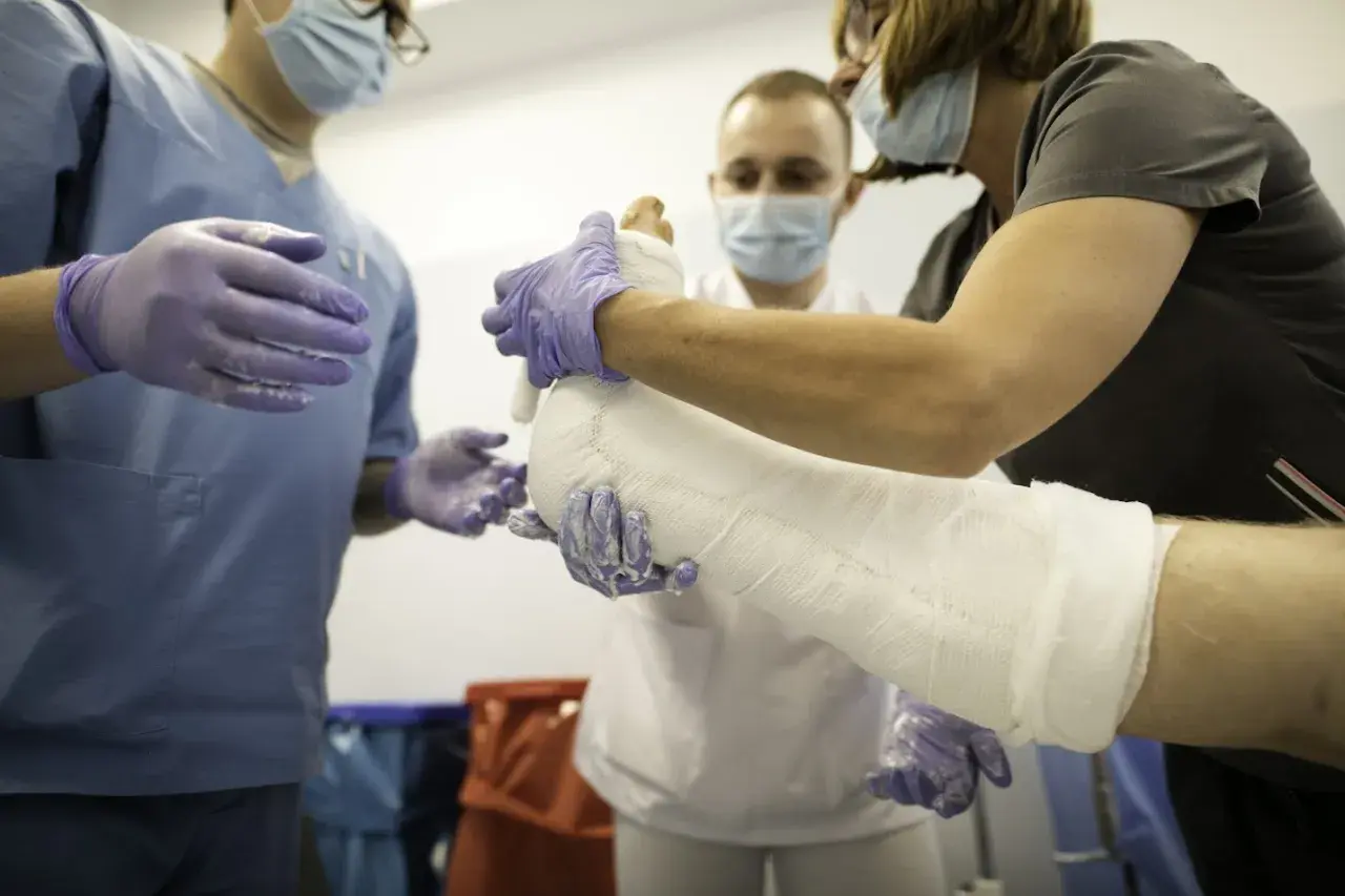 Trzech lekarzy w maseczkach i rękawiczkach zakłada gips na nogę pacjenta.