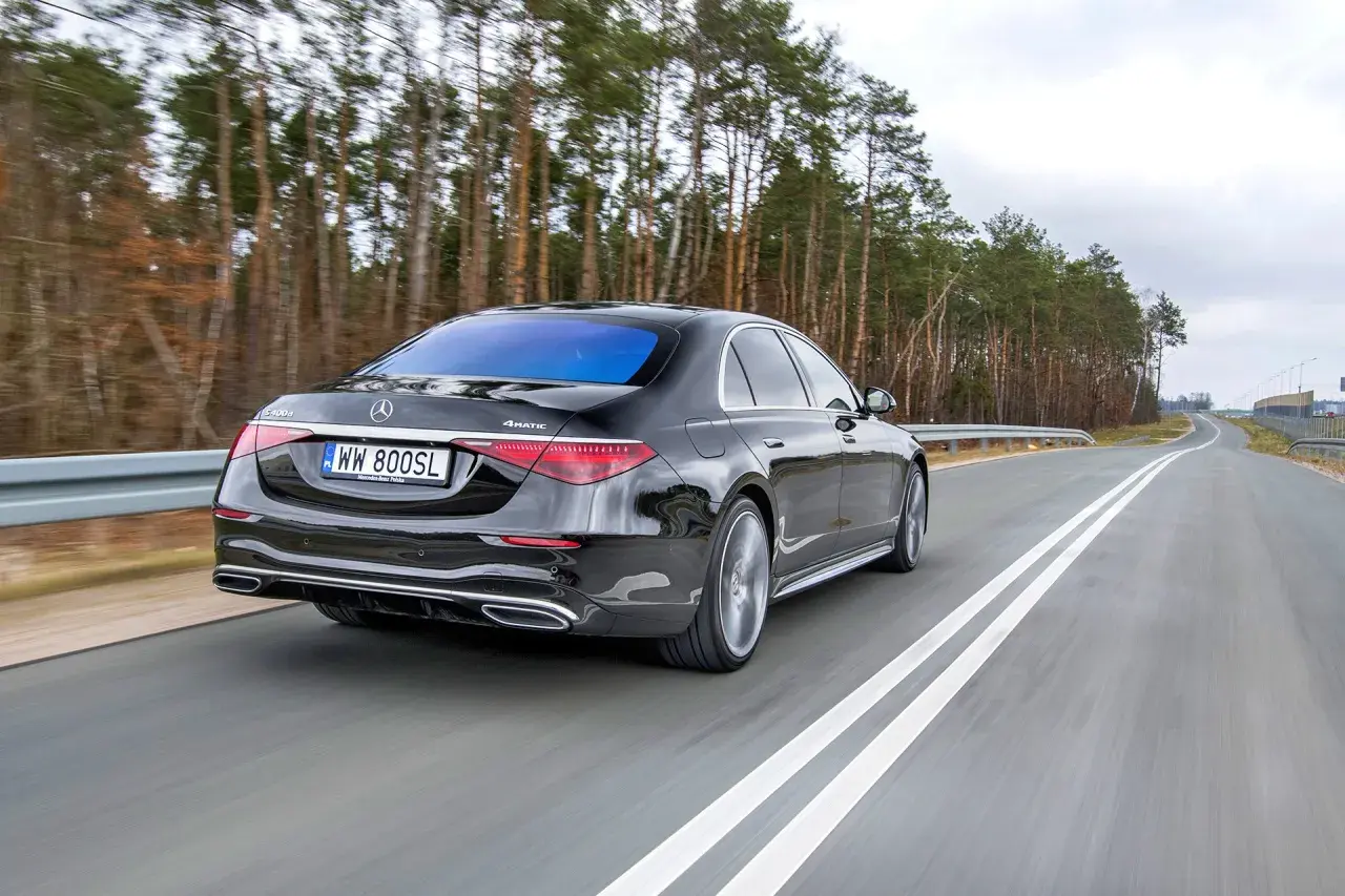 Czarny Mercedes S400d 4Matic sunie po drodze wśród drzew.