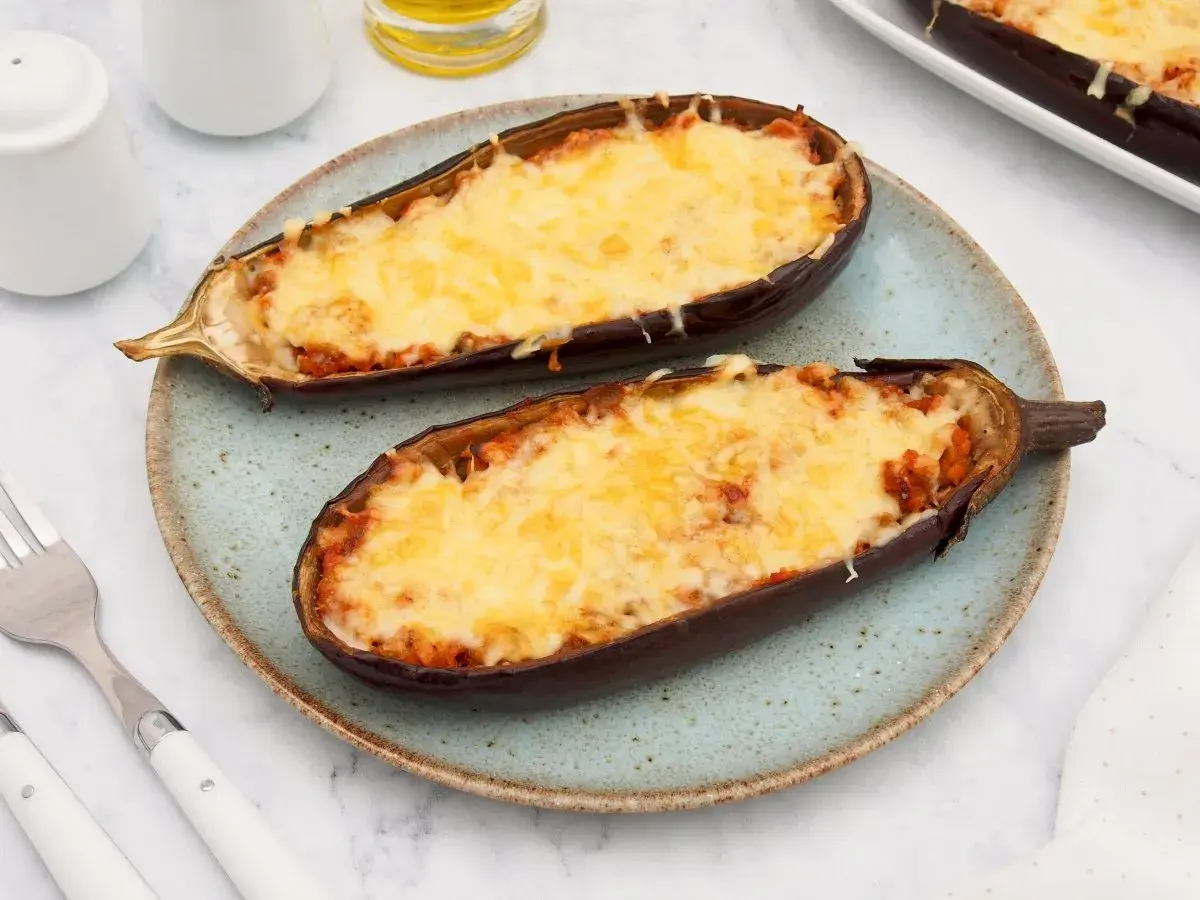 Dos mitades de berenjenas rellenas de atún, gratinadas con queso derretido, servidas en un plato azul.
