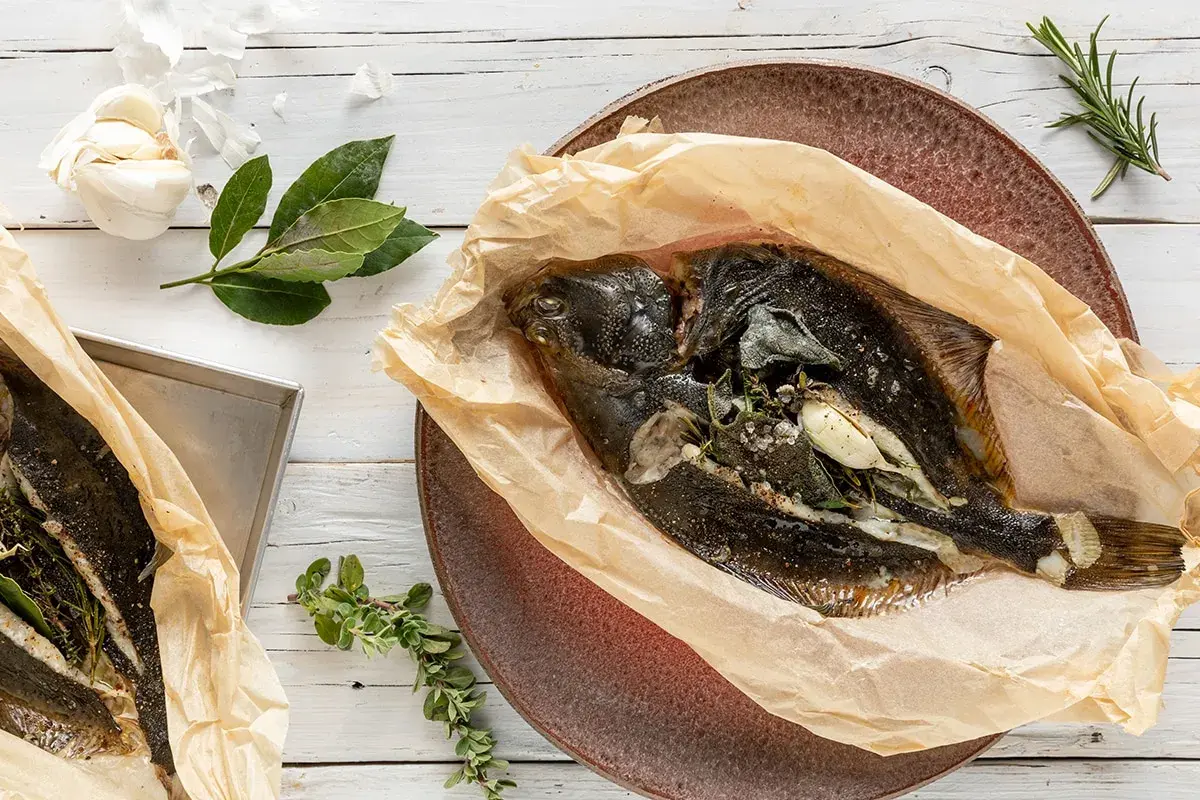 Two whole sole fish, seasoned and wrapped in parchment paper, with garlic and herbs.