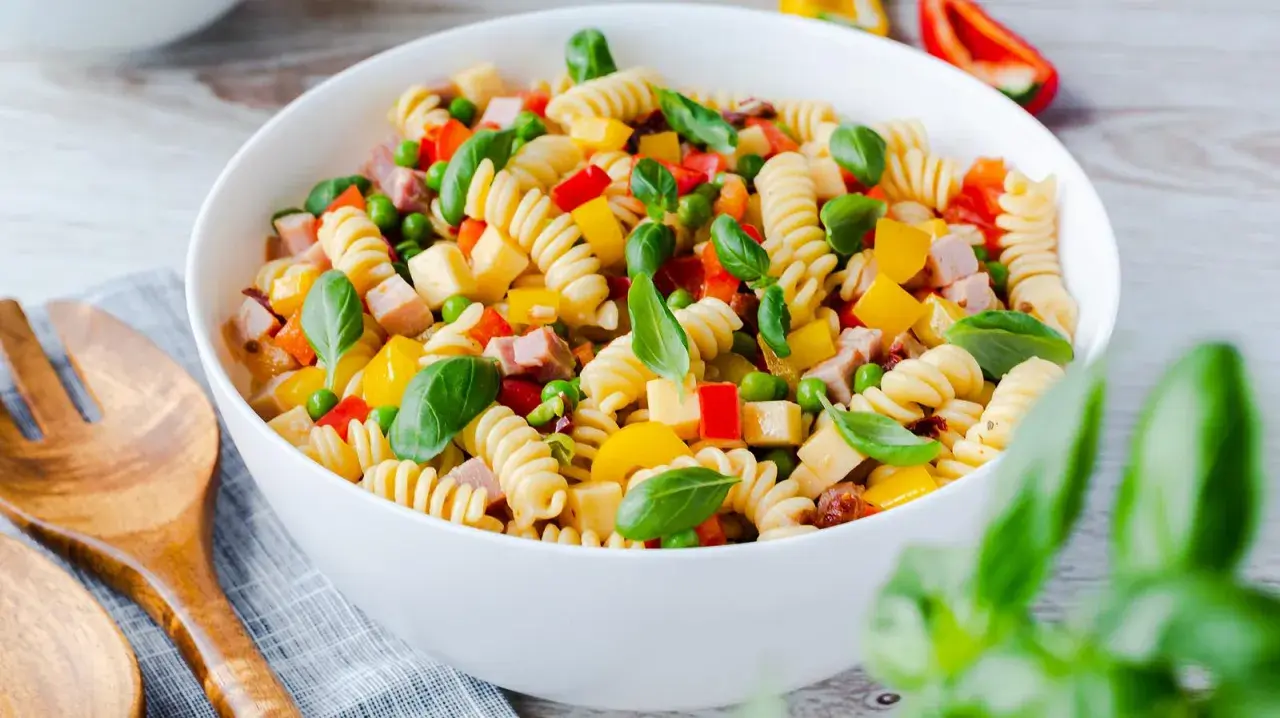 Bunter Nudelsalat ohne Mayo mit Spiralnudeln, Erbsen, Paprika und Schinkenwürfeln, garniert mit Basilikum.