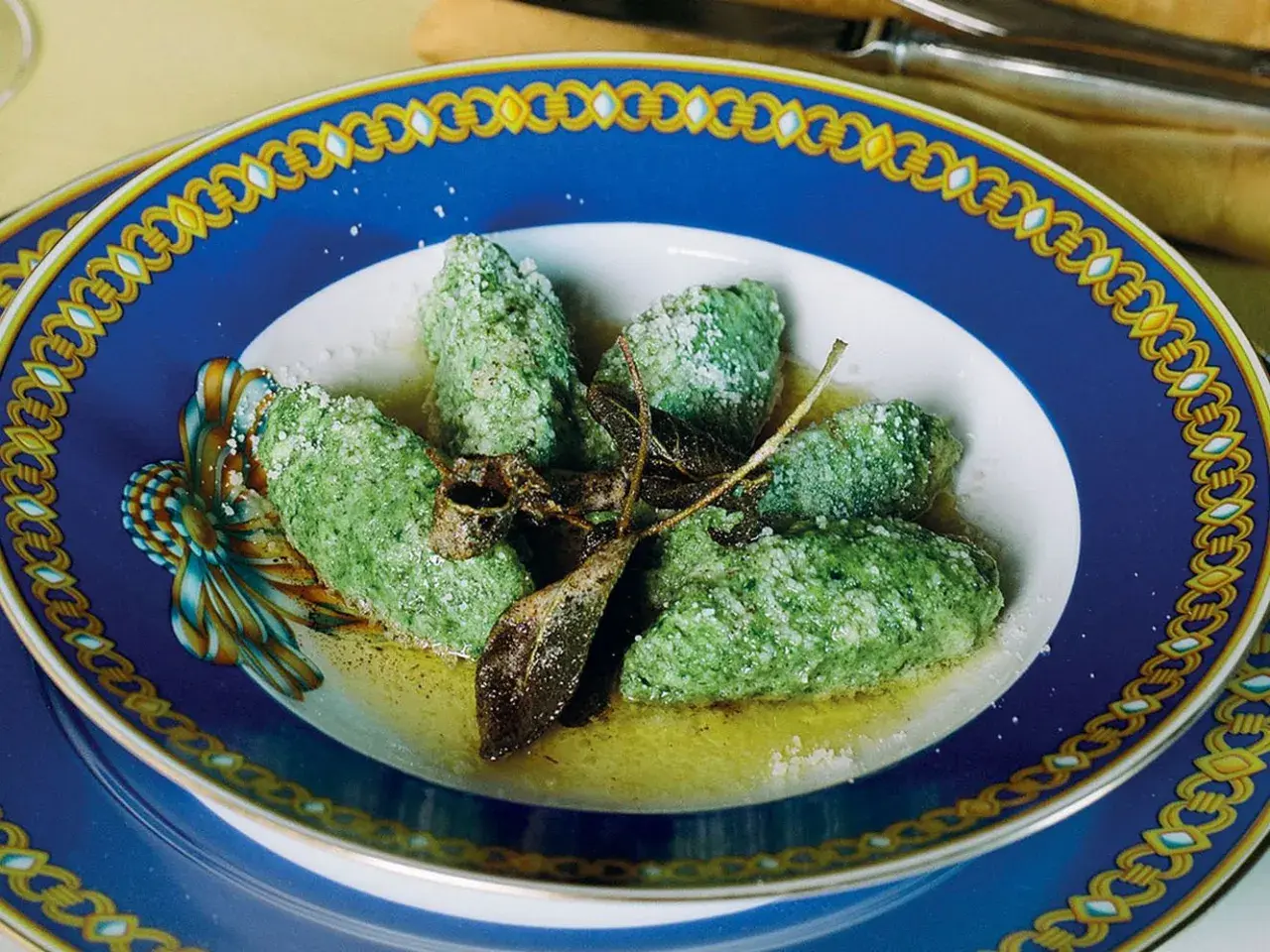 Strangolapreti alla trentina, verdi e saporiti, serviti in un piatto elegante con burro fuso e salvia croccante.