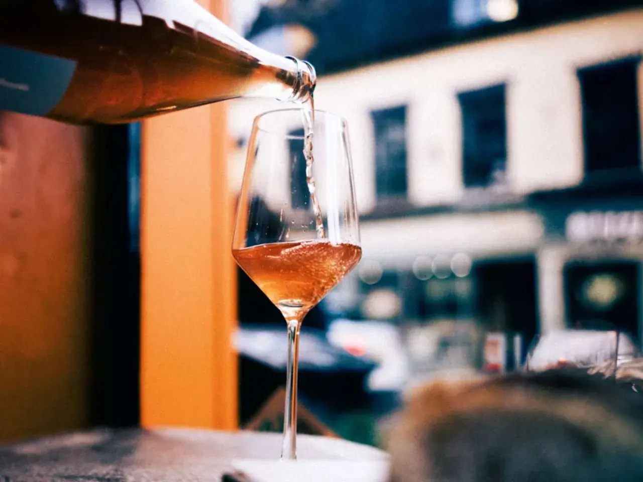 En flaska häller upp ett bubbligt, roséfärgat pet nat i ett elegant glas. En härlig kväll väntar.