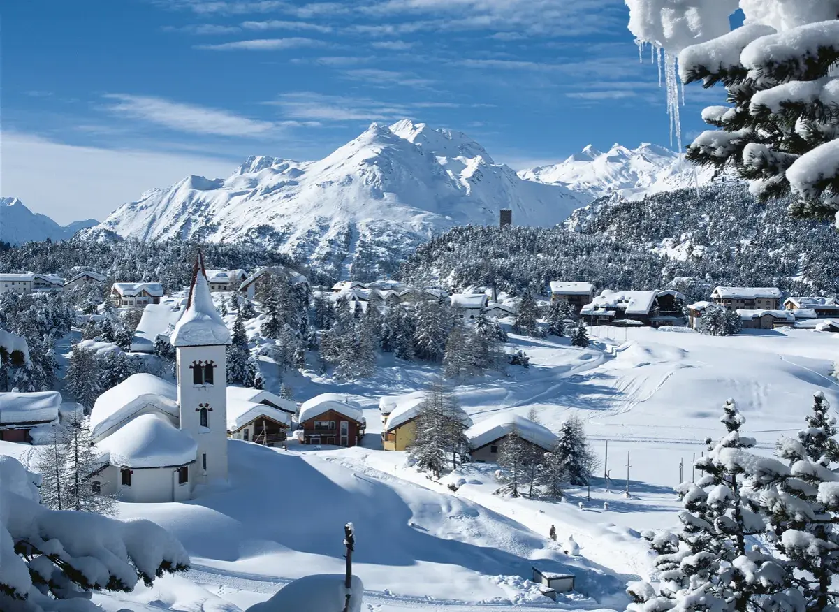 Winteridylle in der Schweiz: verschneite Berge, ein Dorf mit Kirche und Häusern, umgeben von Tannen.