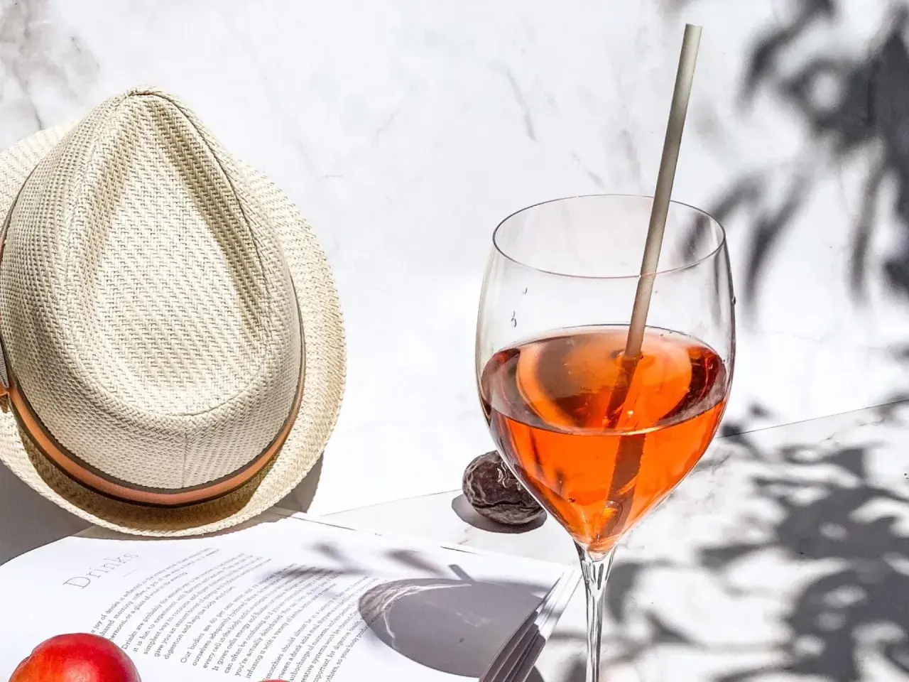 Ein Aperol Spritz im Glas neben einem Strohhut und einem Buch.
