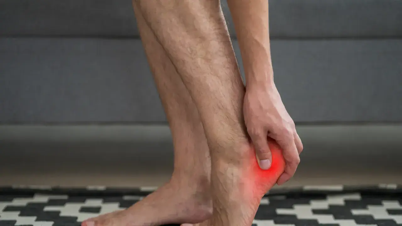 Hombre tocando su talón con un punto rojo que indica dolor en el talón del pie.