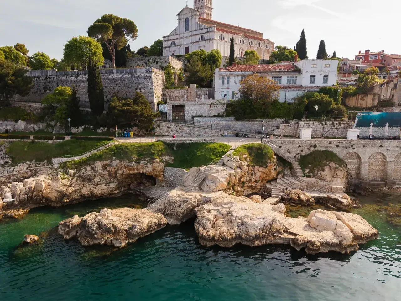 Felsige Küste mit kristallklarem Wasser und einer Kirche auf dem Hügel. Entdecke Rovinj Geheimtipps abseits der Touristenpfade.