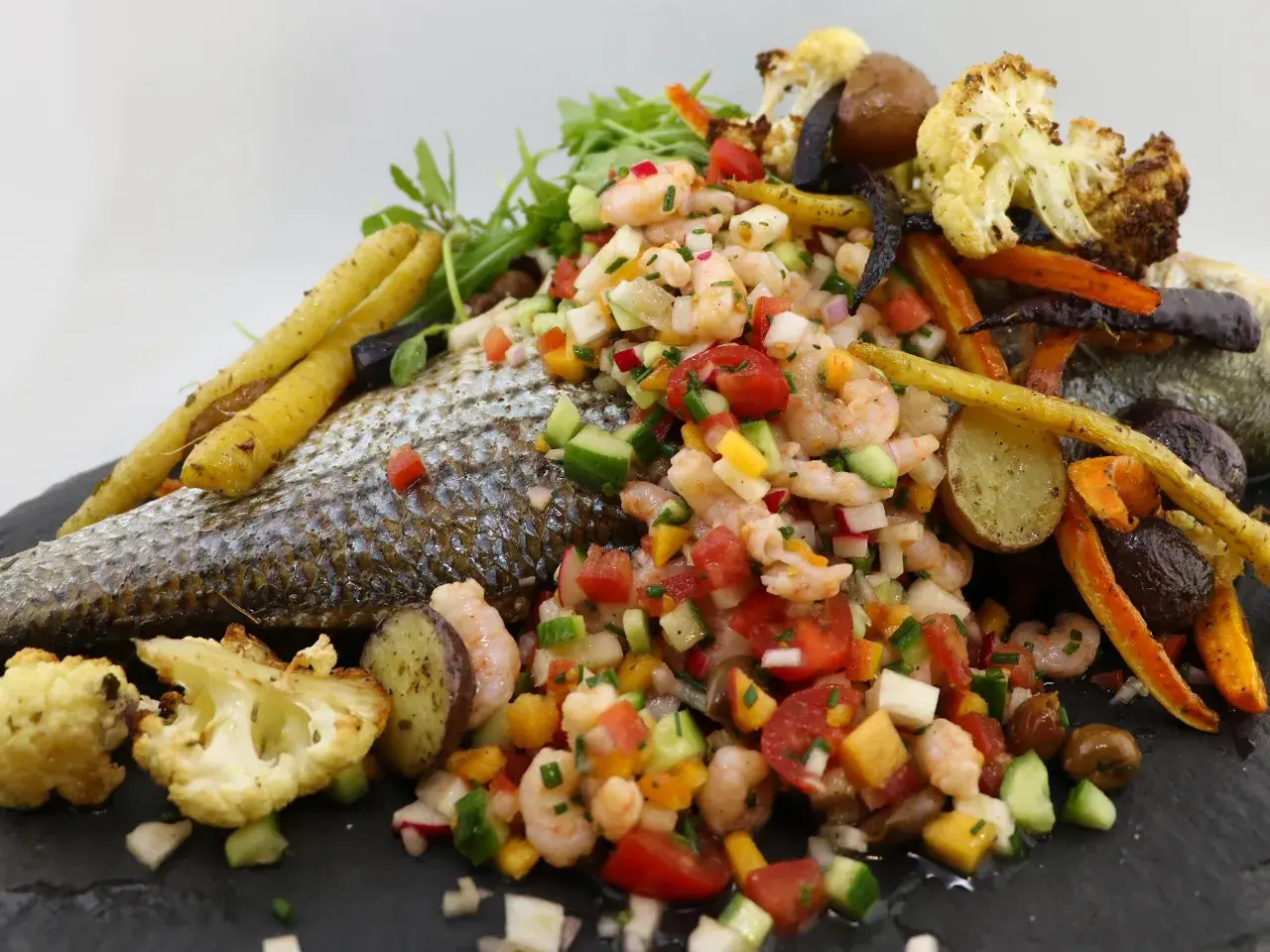 Poisson au barbecue avec salade de crevettes, légumes rôtis et herbes fraîches. Un plat coloré et savoureux.