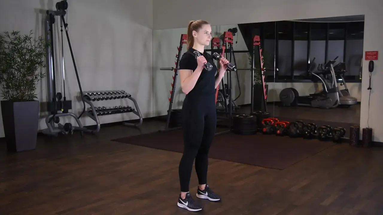 Kobieta wykonuje uginanie ramion z hantlami, ćwicząc bicepsy w siłowni.