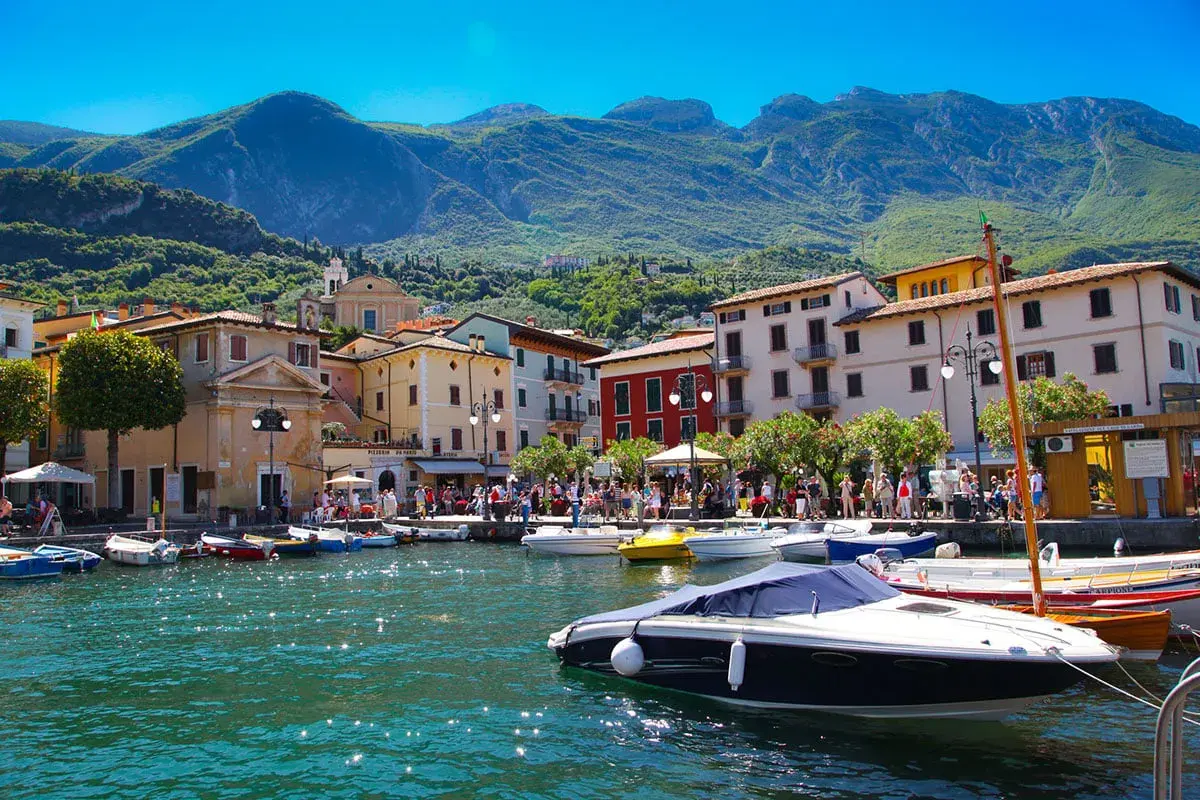 Barche ormeggiate nel porto di Salò, sul Lago di Garda, con case colorate e montagne verdi sullo sfondo.
