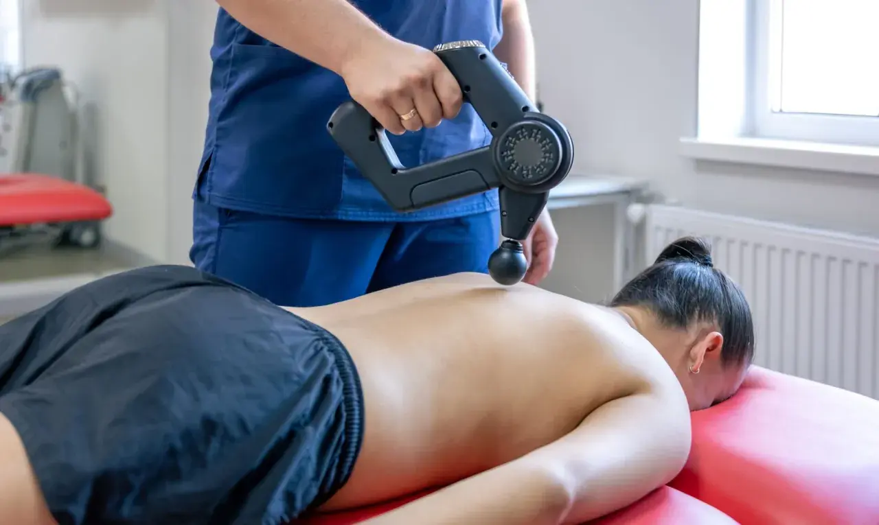 Fizjoterapeuta wykonuje masaż wibracyjny pleców. Choć zazwyczaj przynosi ulgę, warto pamiętać o potencjalnych masaż wibracyjny skutki uboczne.