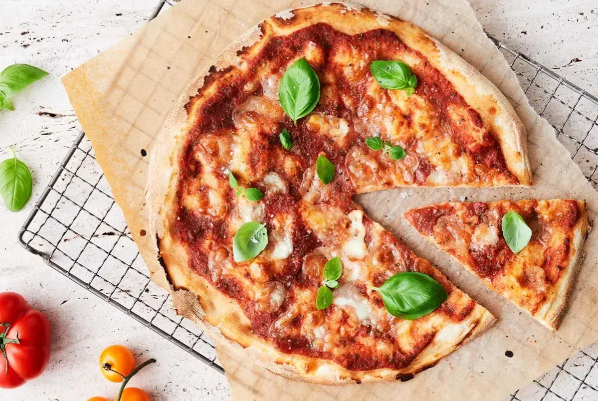 En nybakad pizza med tomatsås, ost och basilika. En bit är bortskuren, perfekt för att njuta av goda pizza kalorier.