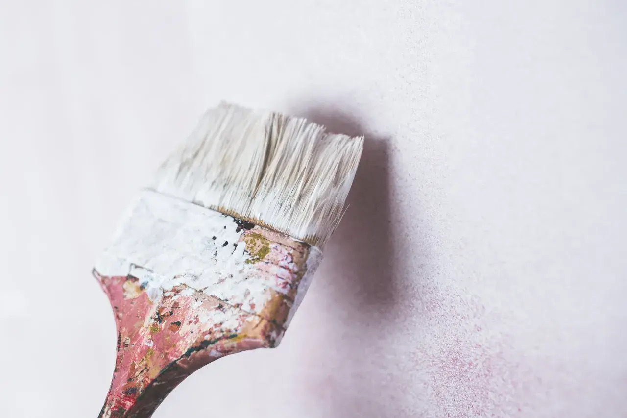 Brocha desgastada con pintura blanca lista para renovar una pared. Se puede pintar encima de pintura de caucho.