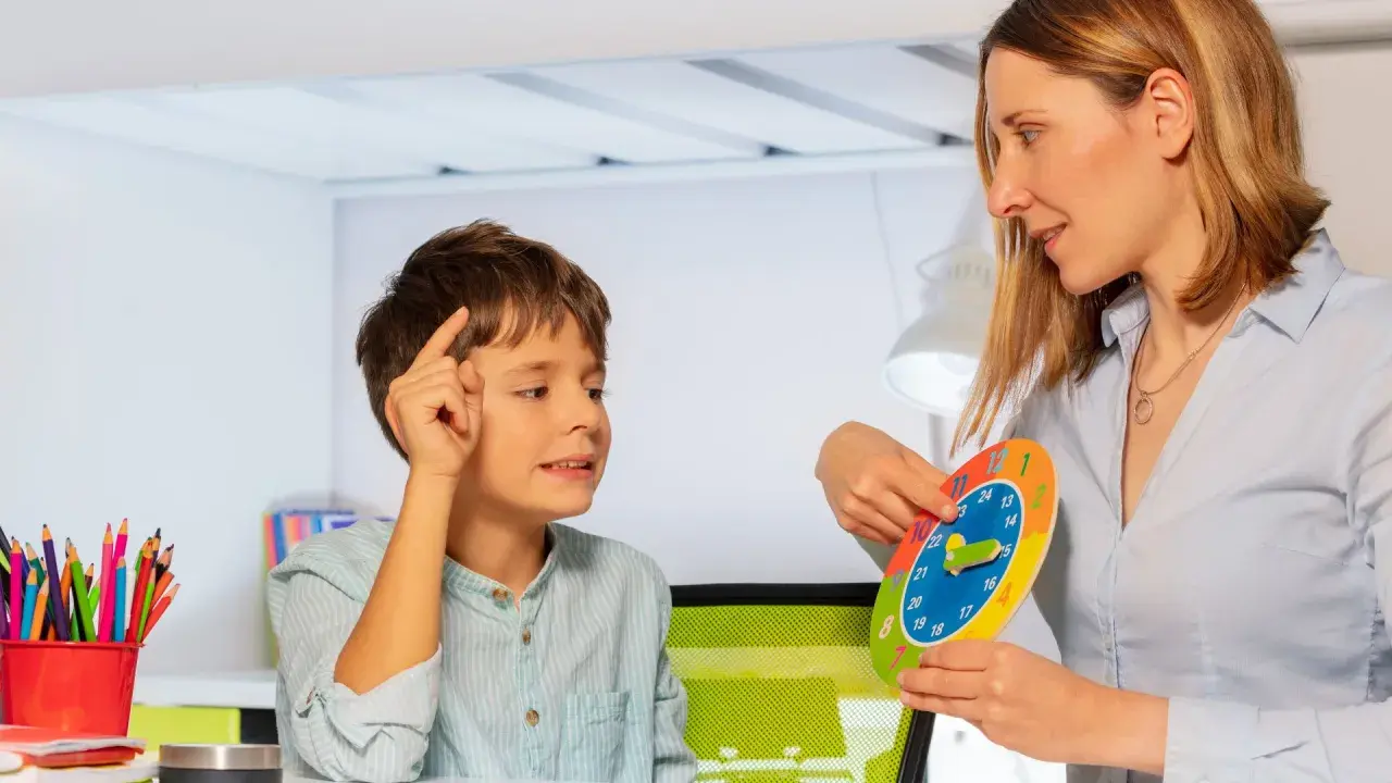 Bambino impara a leggere l'ora con una terapista occupazionale che usa un orologio colorato.