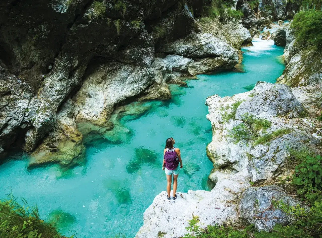 Wanderin am Juliana Trail: Eine Frau mit Rucksack steht auf einem Felsen und blickt auf das türkisfarbene Wasser einer Schlucht.