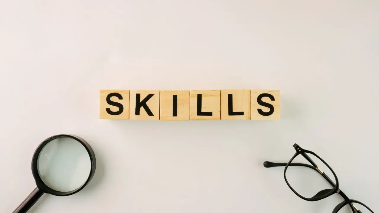 Wooden blocks spell "SKILLS." A magnifying glass and glasses suggest an organization leader carefully assessing talents.