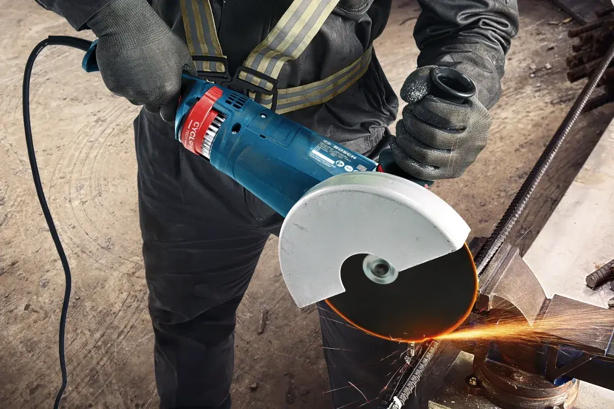 Pracownik w rękawicach zakłada tarczę na szlifierkę kątową Bosch, przygotowując się do cięcia metalu. Iskry sypią się podczas pracy.