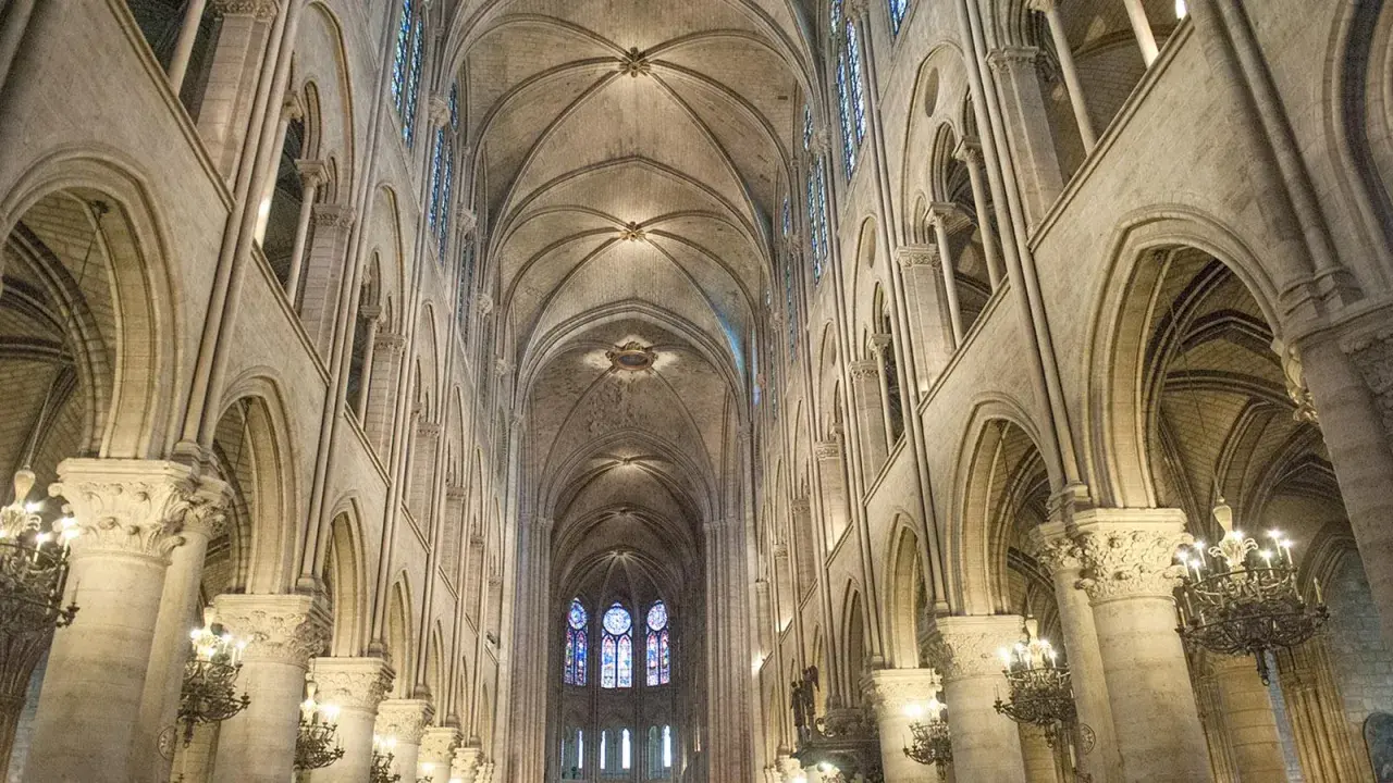 Das Innere der Notre Dame erstreckt sich mit seinen gotischen Bögen und Gewölben in die Höhe. Buntglasfenster erhellen den Raum.