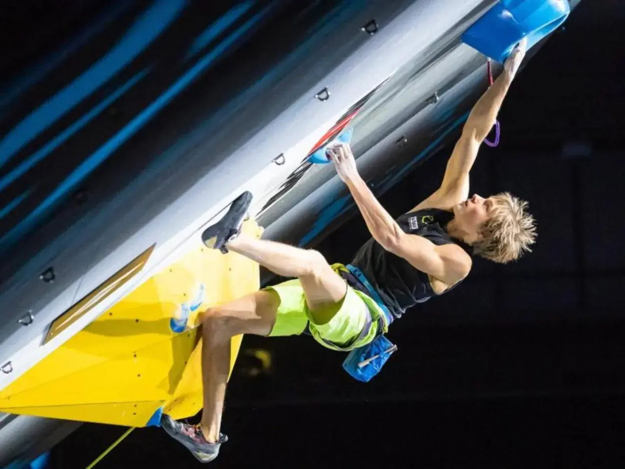 Alex Megos kämpft sich an einer Kletterwand hoch, seine Muskeln angespannt.