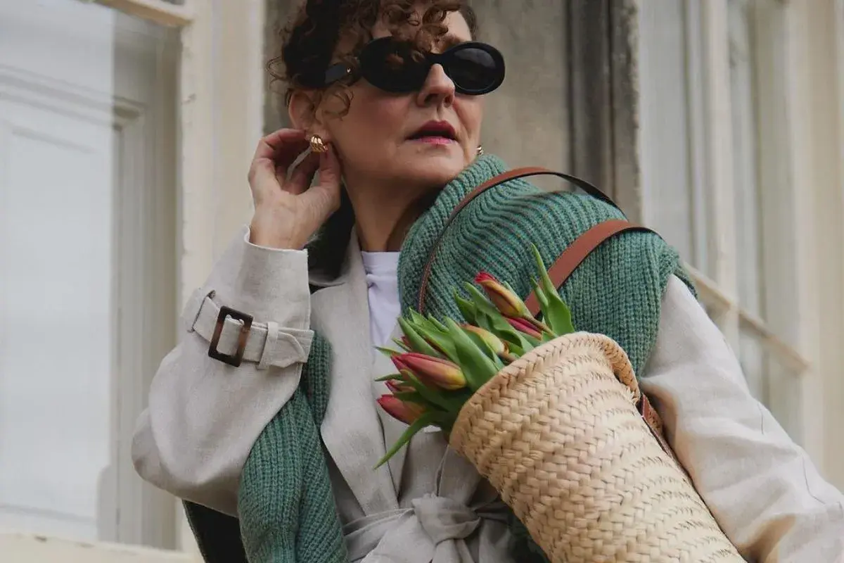 Elegancka kobieta w okularach i płaszczu, z koszykiem pełnym tulipanów. Uosobienie stylu francuskiego w modzie damskiej.