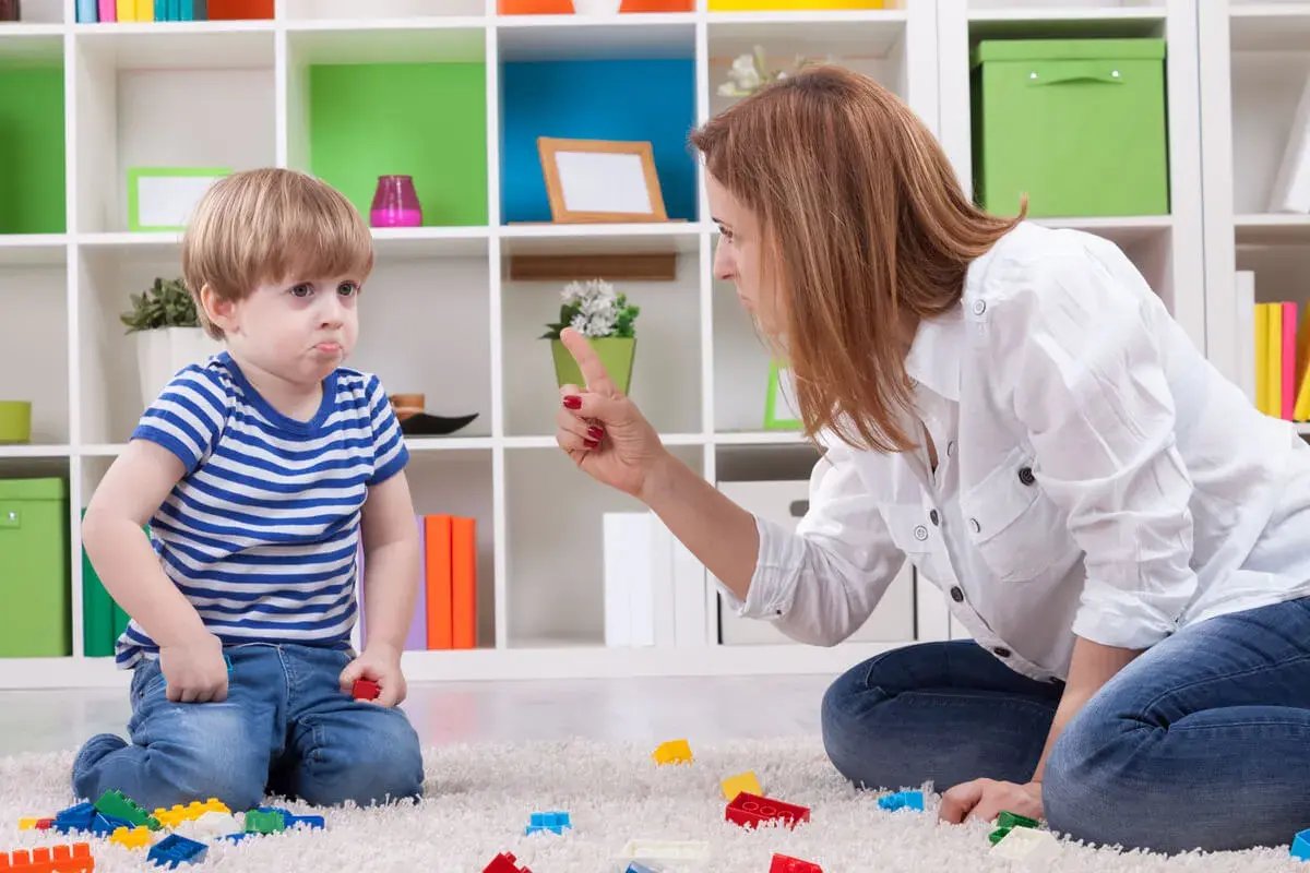 Niño con cara de enfado, actitud negativista desafiante, mientras su madre le regaña.