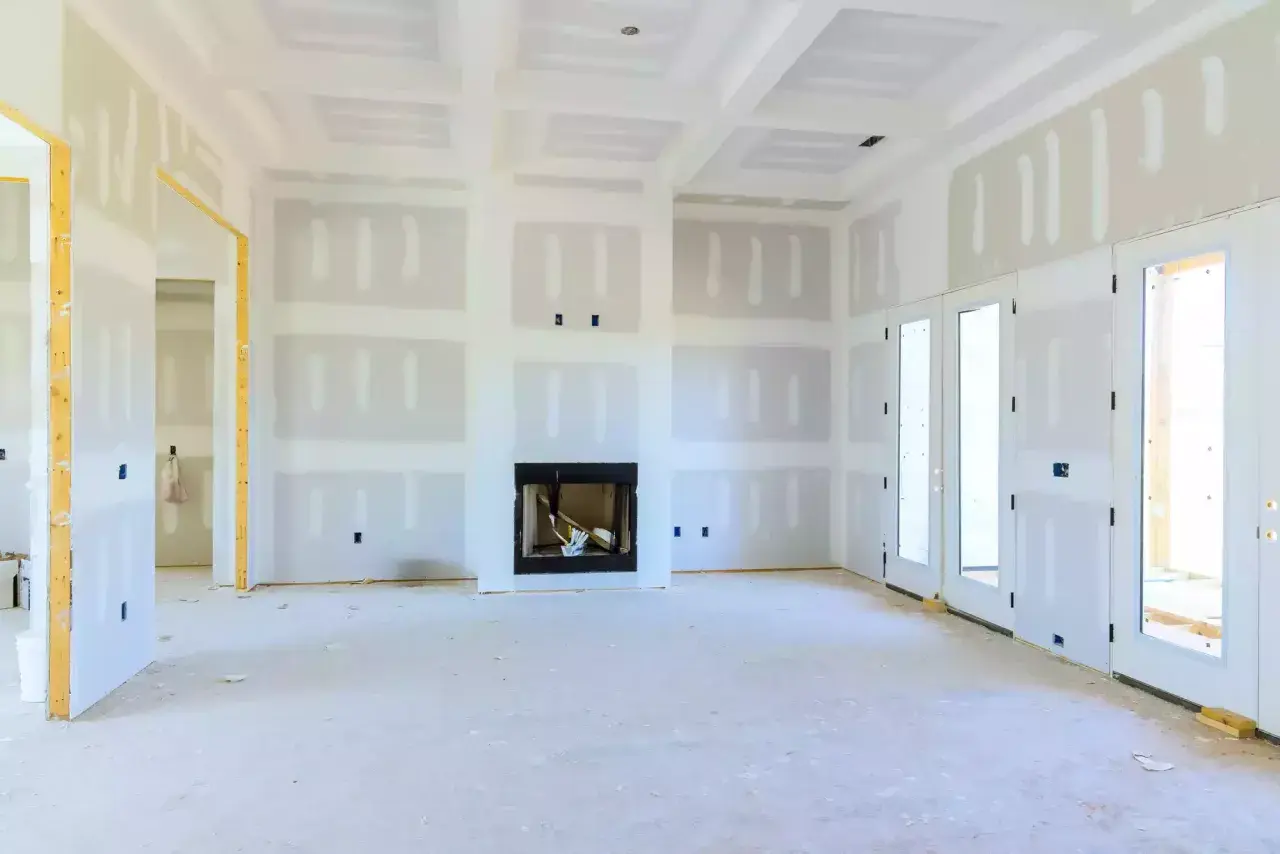 Interno di una casa in costruzione, con pareti e soffitto in cartongesso, camino e porte finestre.