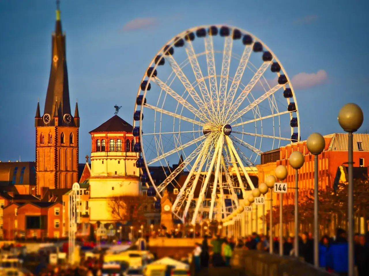 Zachód słońca nad Renem, gdzie dusseldorf atrakcje, takie jak diabelski młyn i wieża kościelna, tworzą malowniczy krajobraz.