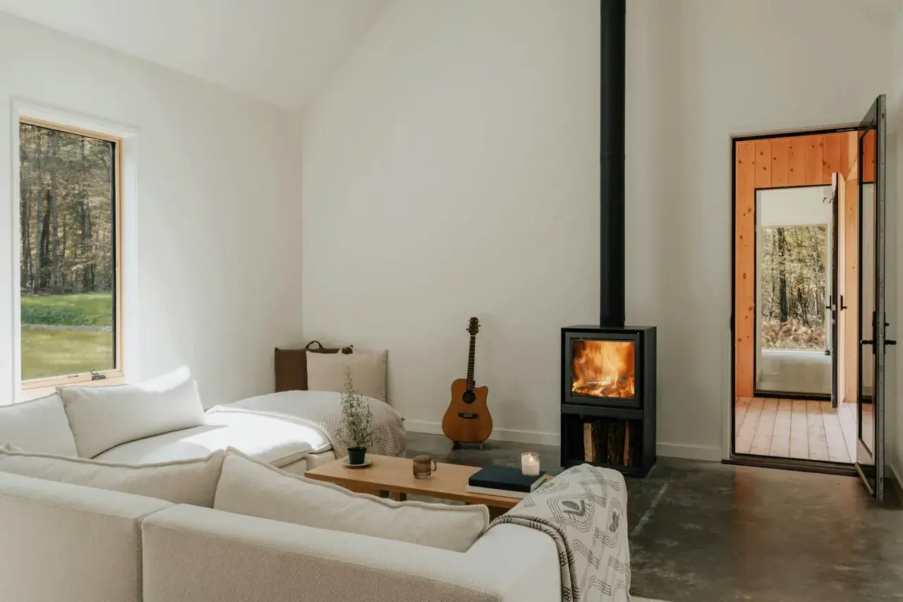 Salon cosy avec poêle à bois allumé, guitare et canapé. Une aide financière pour le tubage de cheminée pourrait rendre ce lieu encore plus chaleureux.
