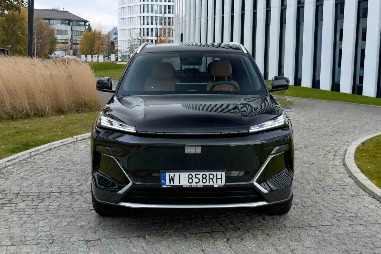 Czarny Geely Coolray z brązowym wnętrzem zaparkowany przed nowoczesnym budynkiem.