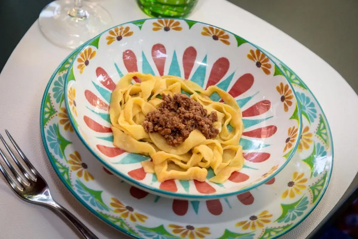 Pyszne tagliatelle al ragu podane w kolorowej miseczce z motywem kwiatowym. Obok leży widelec.