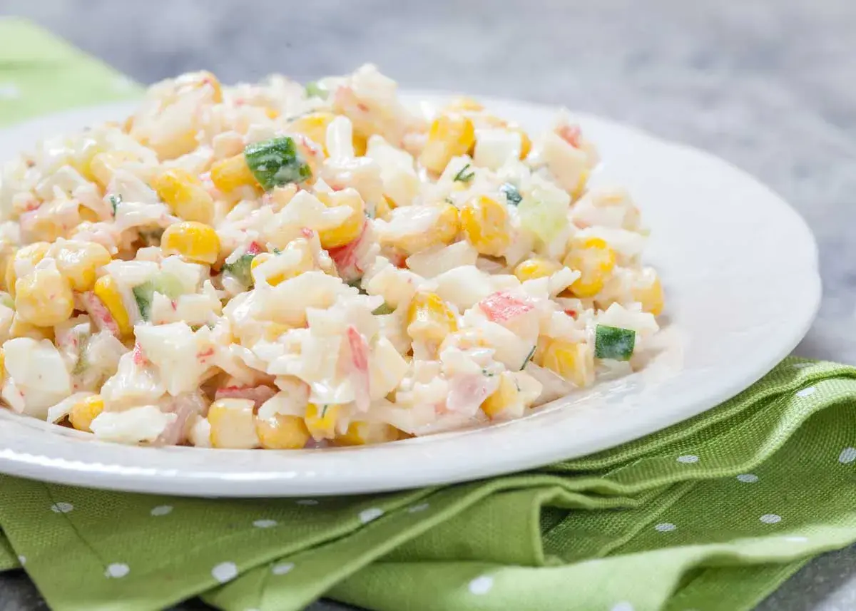 Deliciosa ensalada de arroz con mayonesa, maíz, pepino y surimi, servida en un plato blanco sobre una servilleta verde.