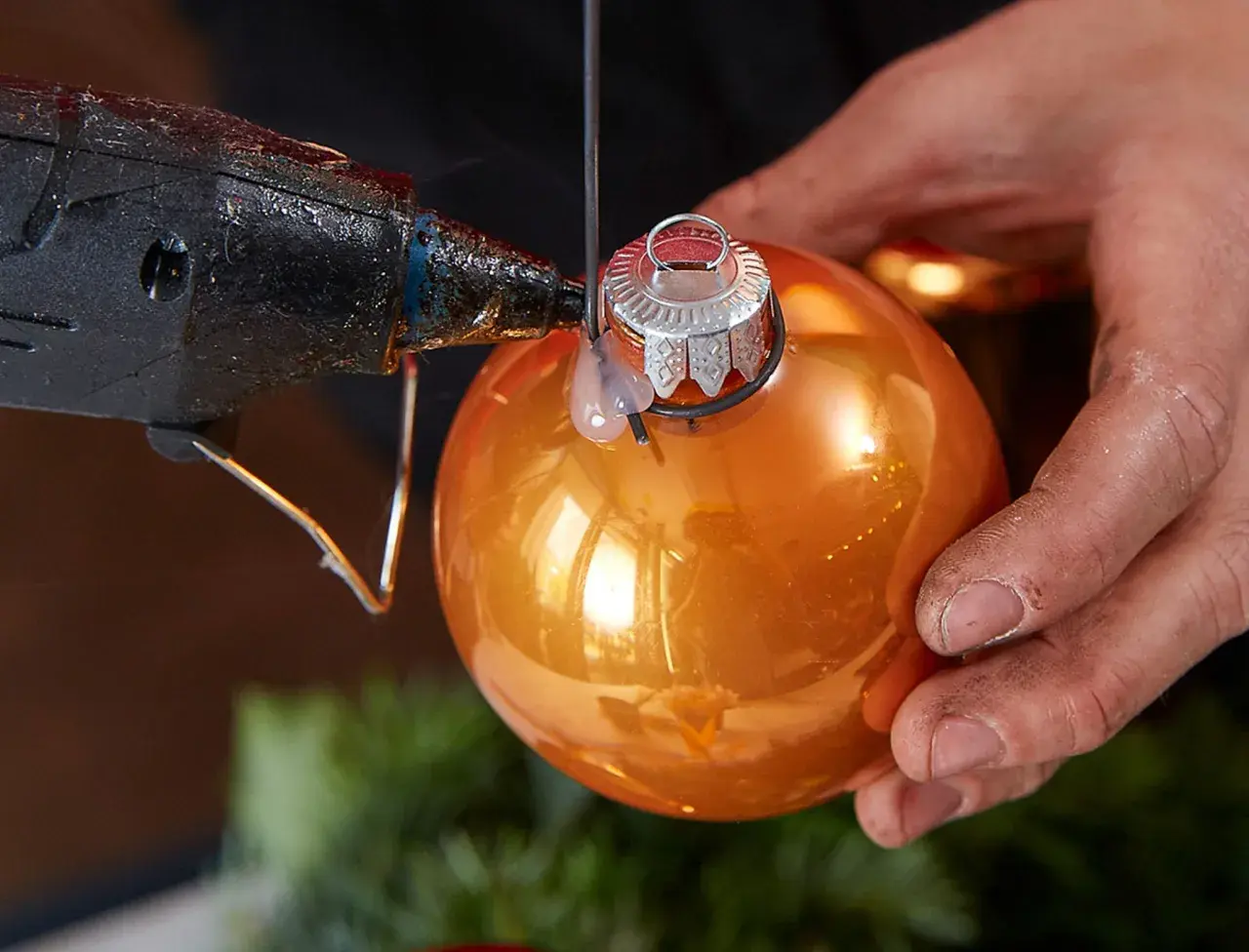 Mit Klebepistole und orangefarbener Kugel einen Adventskranz aus Kugeln selber basteln.