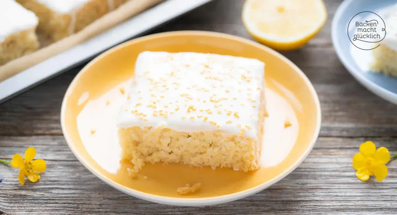 Ein Stück saftiger, veganer Zitronenkuchen mit weißer Glasur und goldenen Streuseln auf einem gelben Teller.