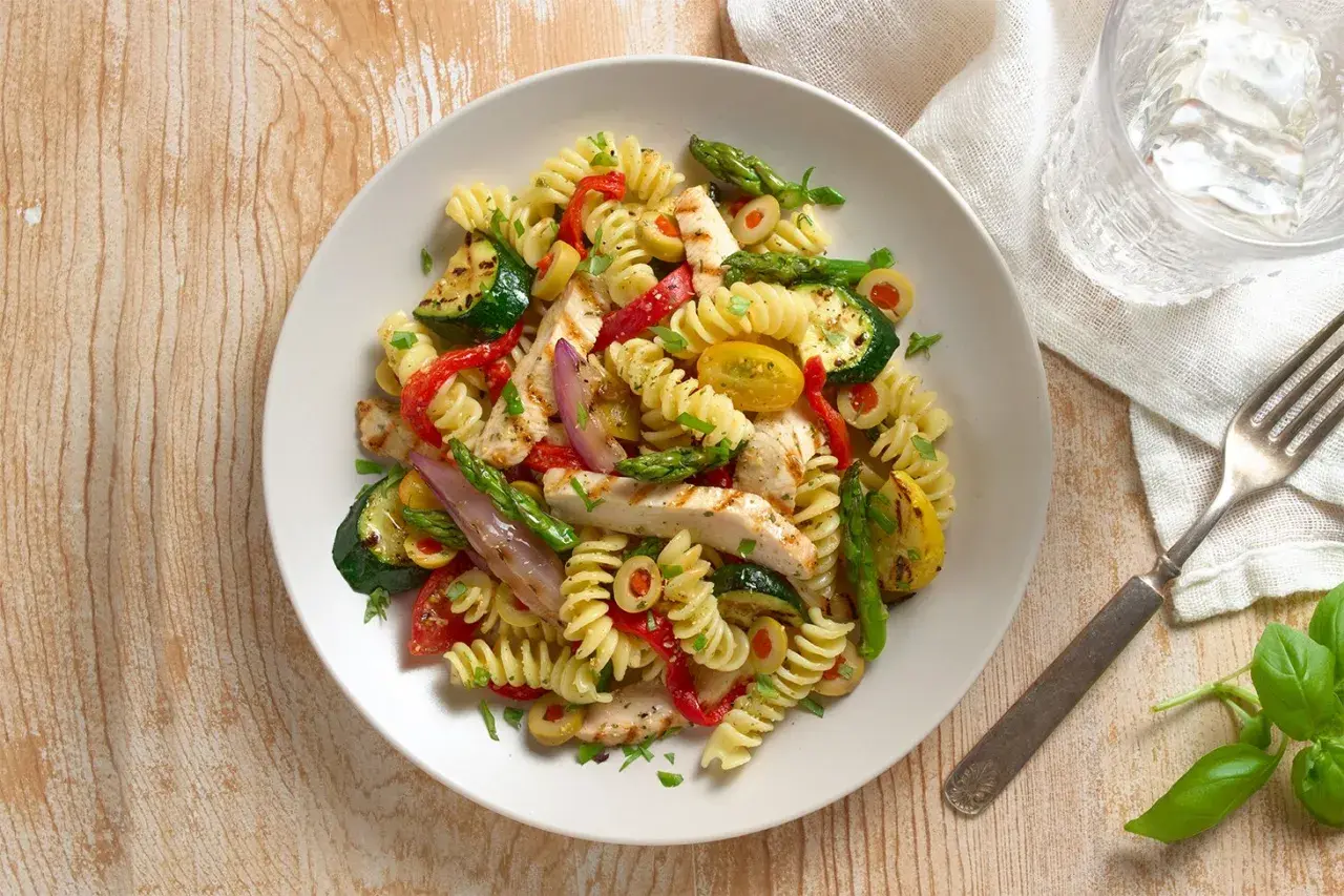 Sabrosa ensalada de pasta con pollo a la parrilla, calabacín, pimientos rojos, espárragos y aceitunas.