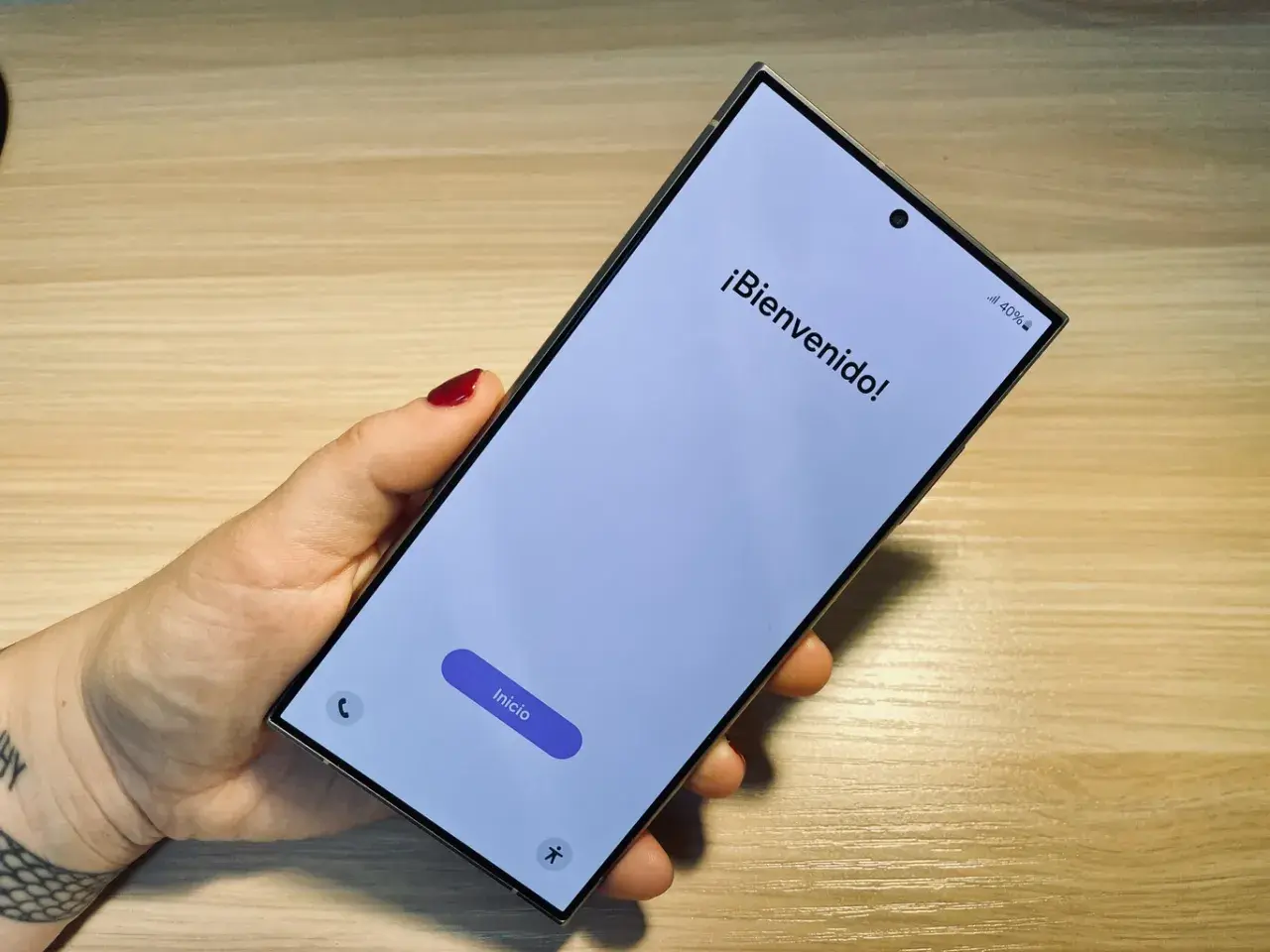 Mano sujetando un móvil listo para formatear. Pantalla de bienvenida con el botón "Inicio" visible.